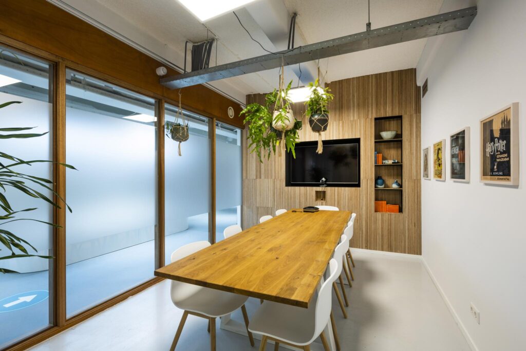 Modern meeting room on Van Diemenstraat with a wooden table, white chairs, hanging plants, and a wall-mounted screen.